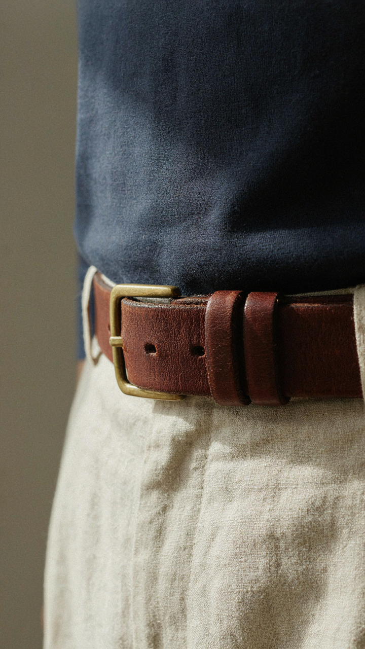 Close-up of a rust leather belt on cream trousers and a navy shirt.