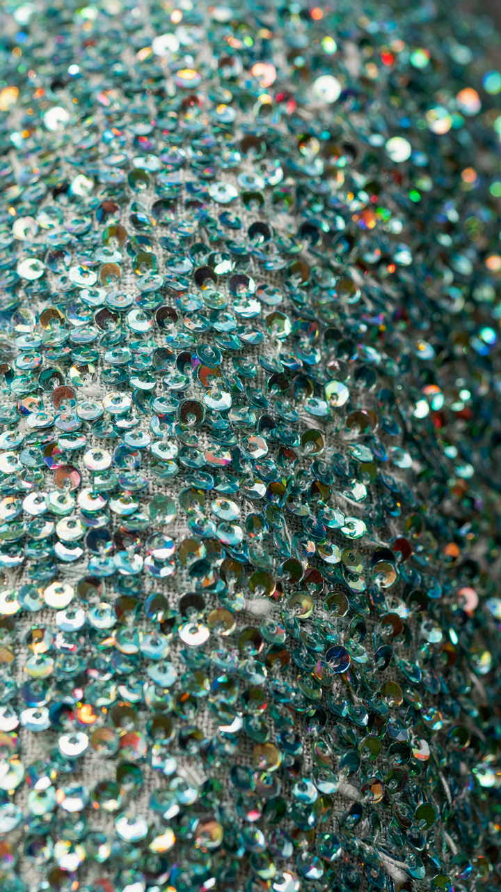 A close up of fine, small sequins shimmering densely on a structured fabric.