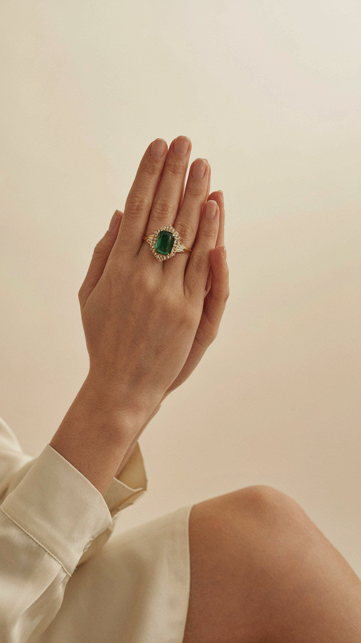 A woman's hand with a single prominent Art Deco statement ring gestures.