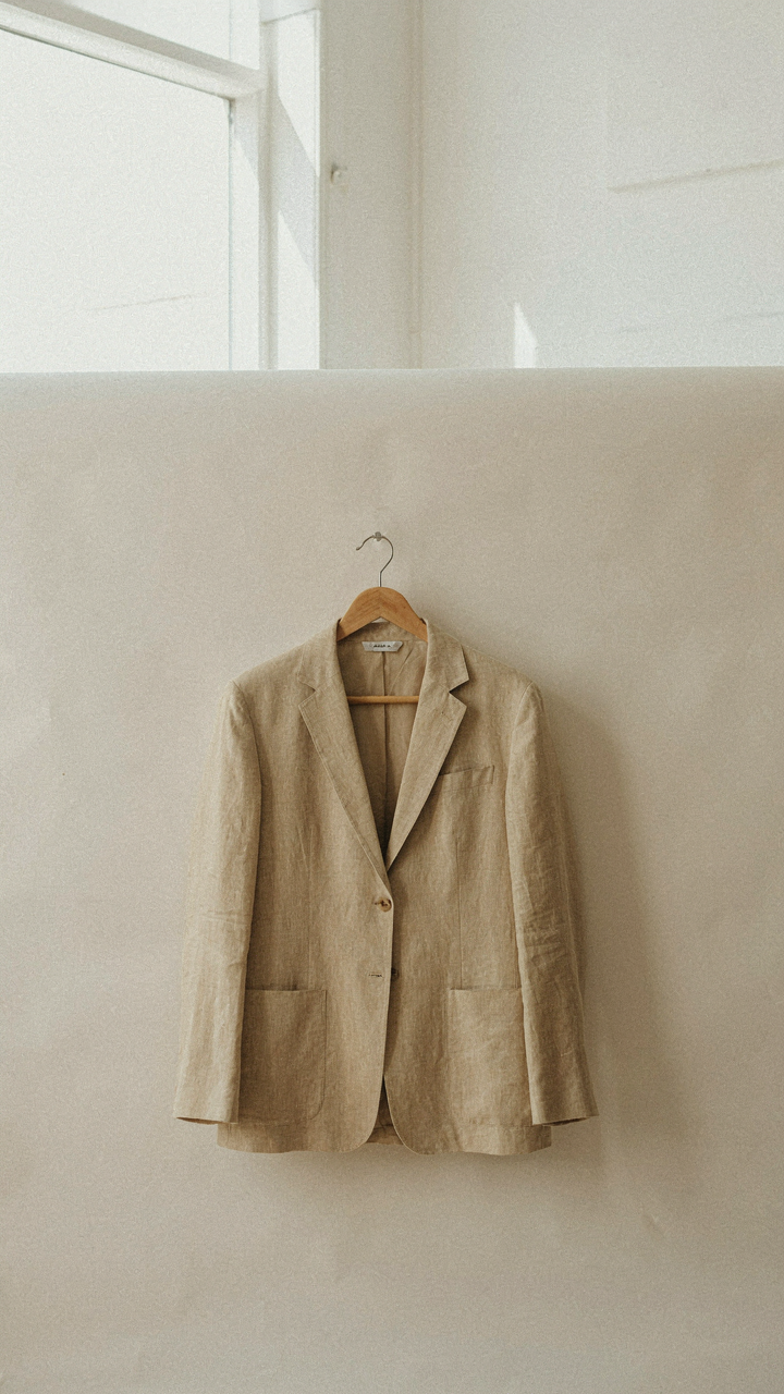 A perfectly tailored linen blazer hangs on a wooden hanger.