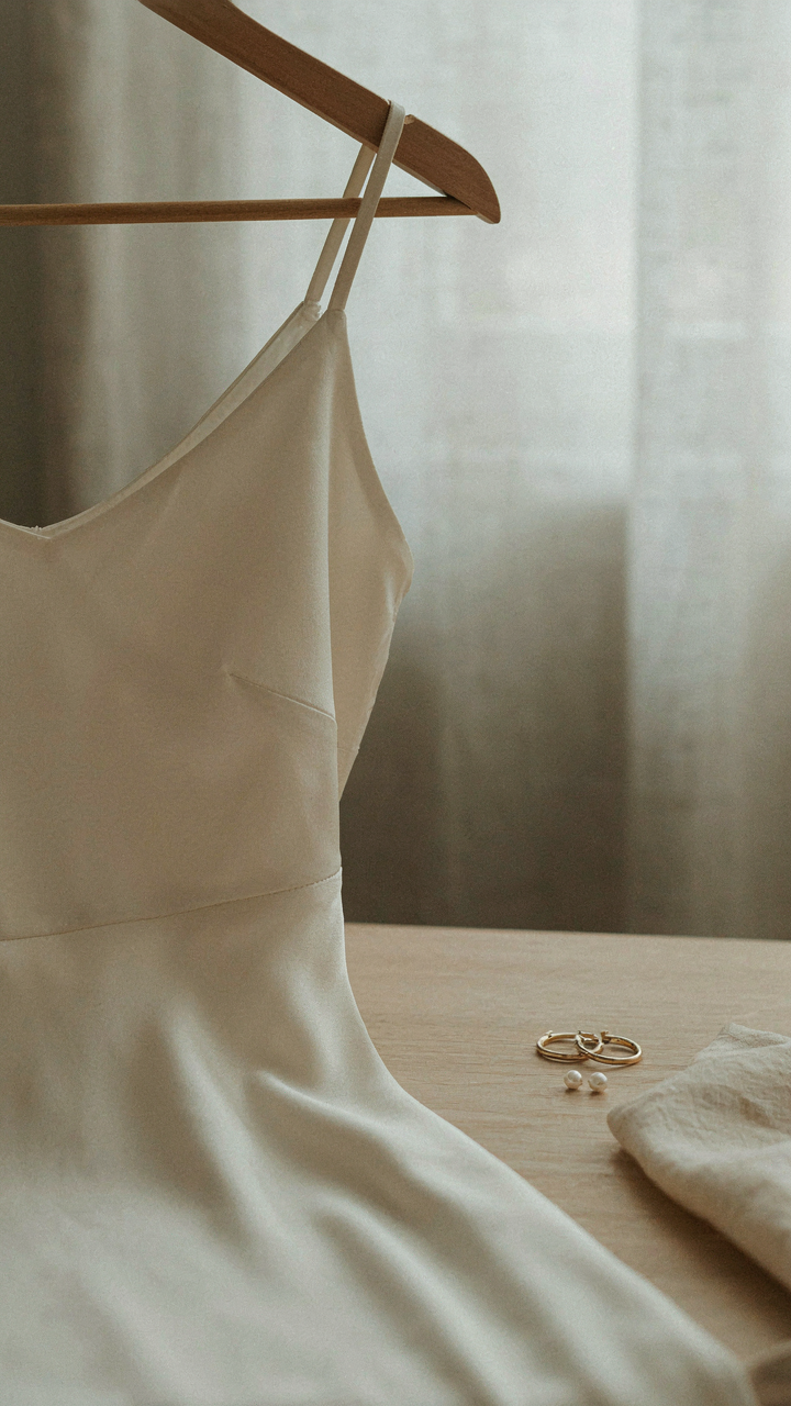 An elegant, solid-colored dress hangs with subtle, delicate earrings beside it.