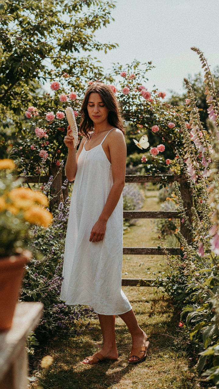 A woman in a loose white linen dress fanning herself outdoors.