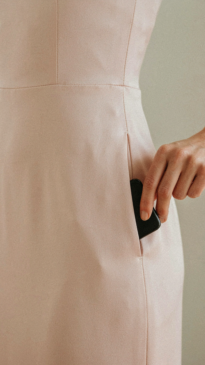 Woman discreetly placing a phone into a side seam pocket of her wedding guest dress.