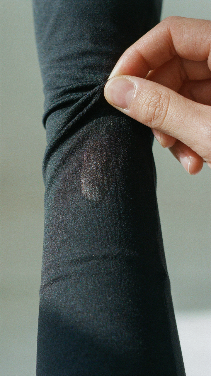 Hand pulling tight synthetic fabric away from sweaty skin.