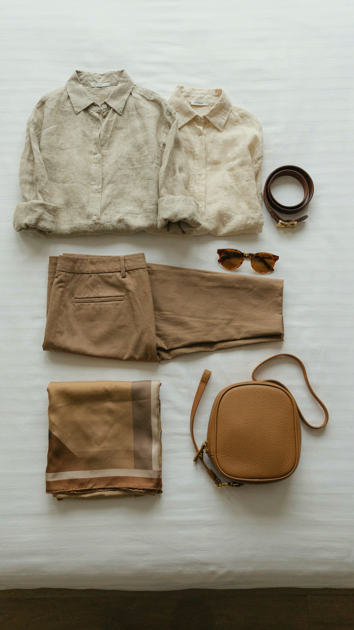 A travel capsule wardrobe laid out on a bed, featuring neutral and versatile items.