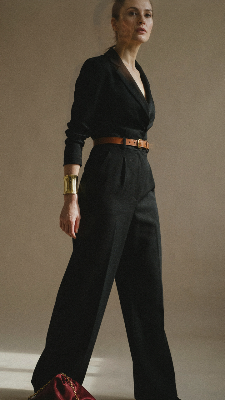 A black jumpsuit is accessorized with a gold cuff and cognac belt.
