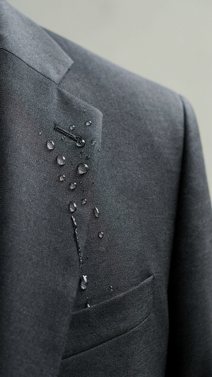 Water beads on the tightly woven surface of a dark, tailored wool-blend blazer.