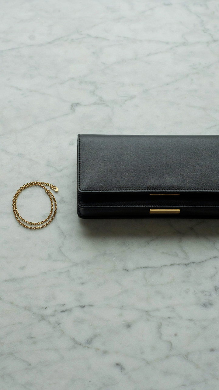 A gold bracelet next to a structured leather clutch, showing balanced contrast.