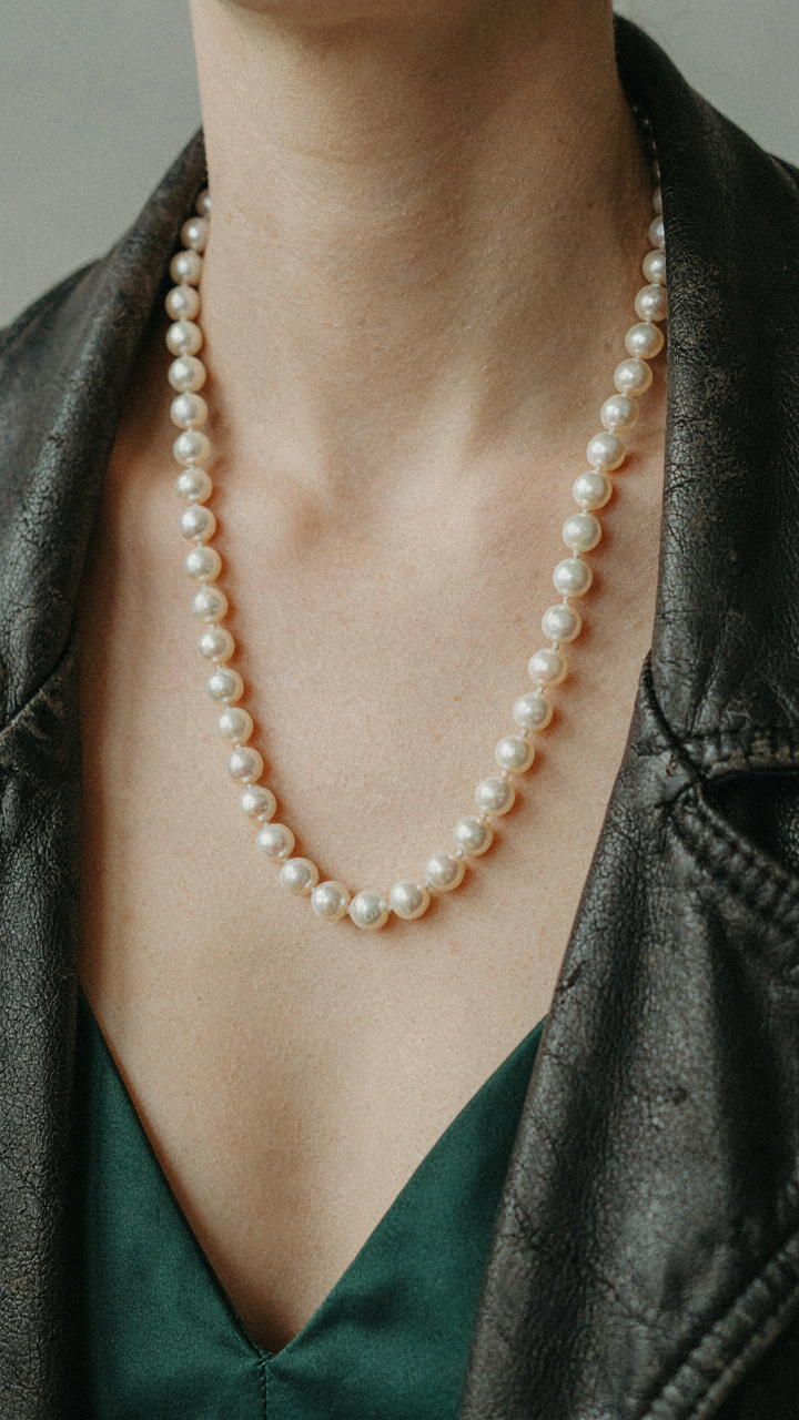 A pearl necklace contrasts with a distressed leather jacket over a dress.