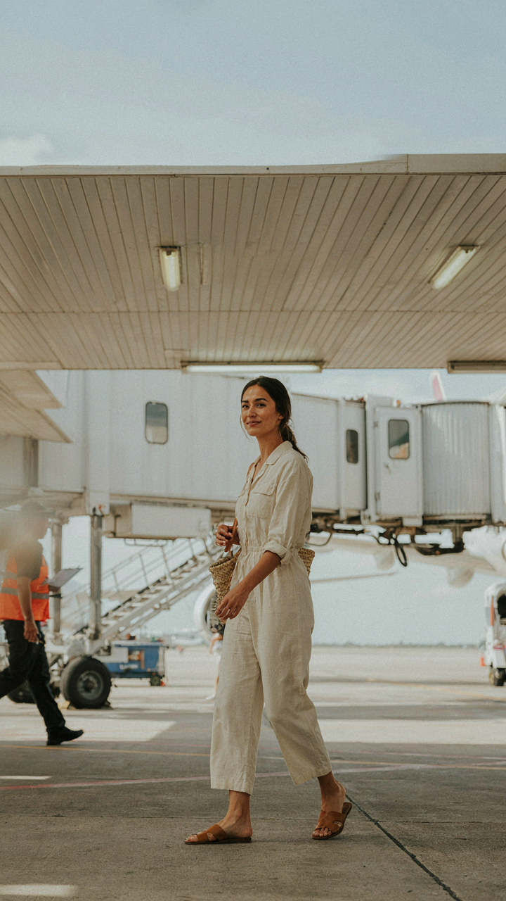 A woman steps off a jet bridge into a sunny destination, her clothes matching the climate.