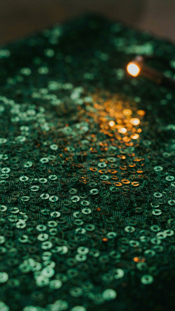 Close-up of sequined fabric reflecting warm light from a lamp.