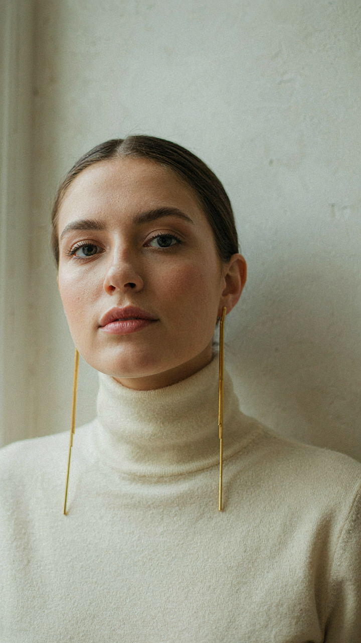 Woman in a high turtleneck wearing long, linear drop earrings.