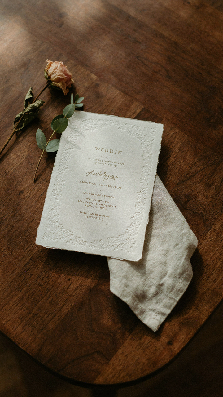 A formal wedding invitation rests on a polished wooden table, detailing dress code.