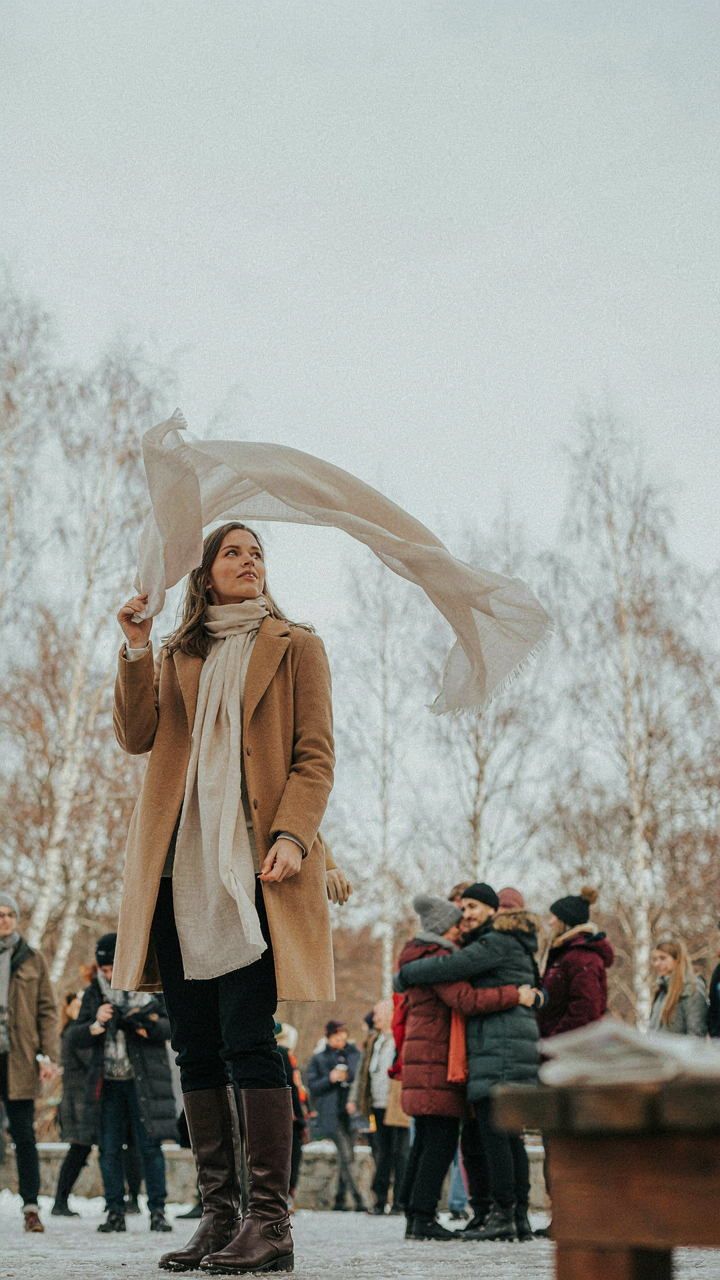 A thin silk scarf drifts in the wind at an outdoor winter event with bundled people.
