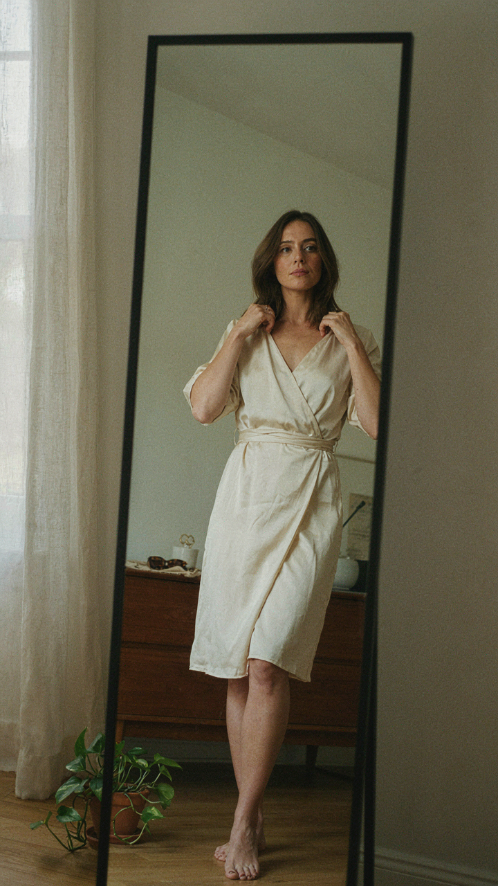 A woman adjusts the V-neckline of her wrap dress in a mirror.