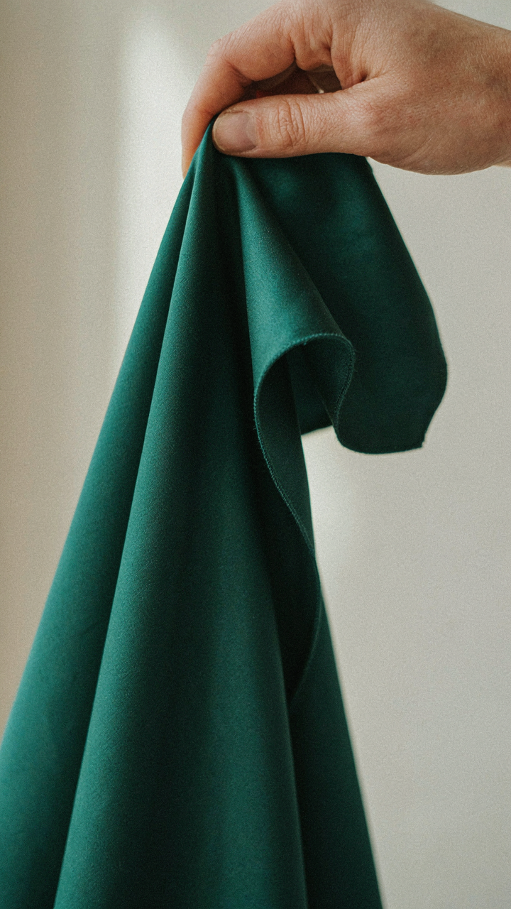 A hand pinches and releases a swatch of silk charmeuse fabric.