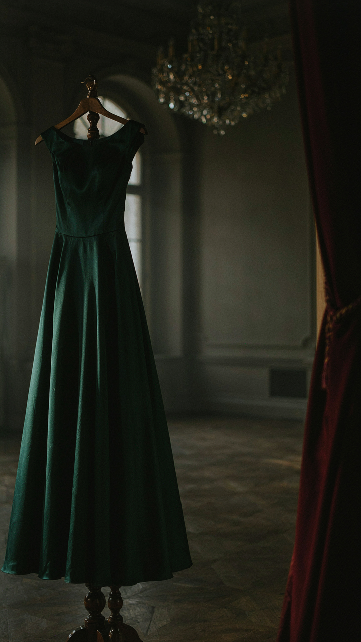 A sophisticated cocktail dress in dark material hangs in an elegant ballroom.
