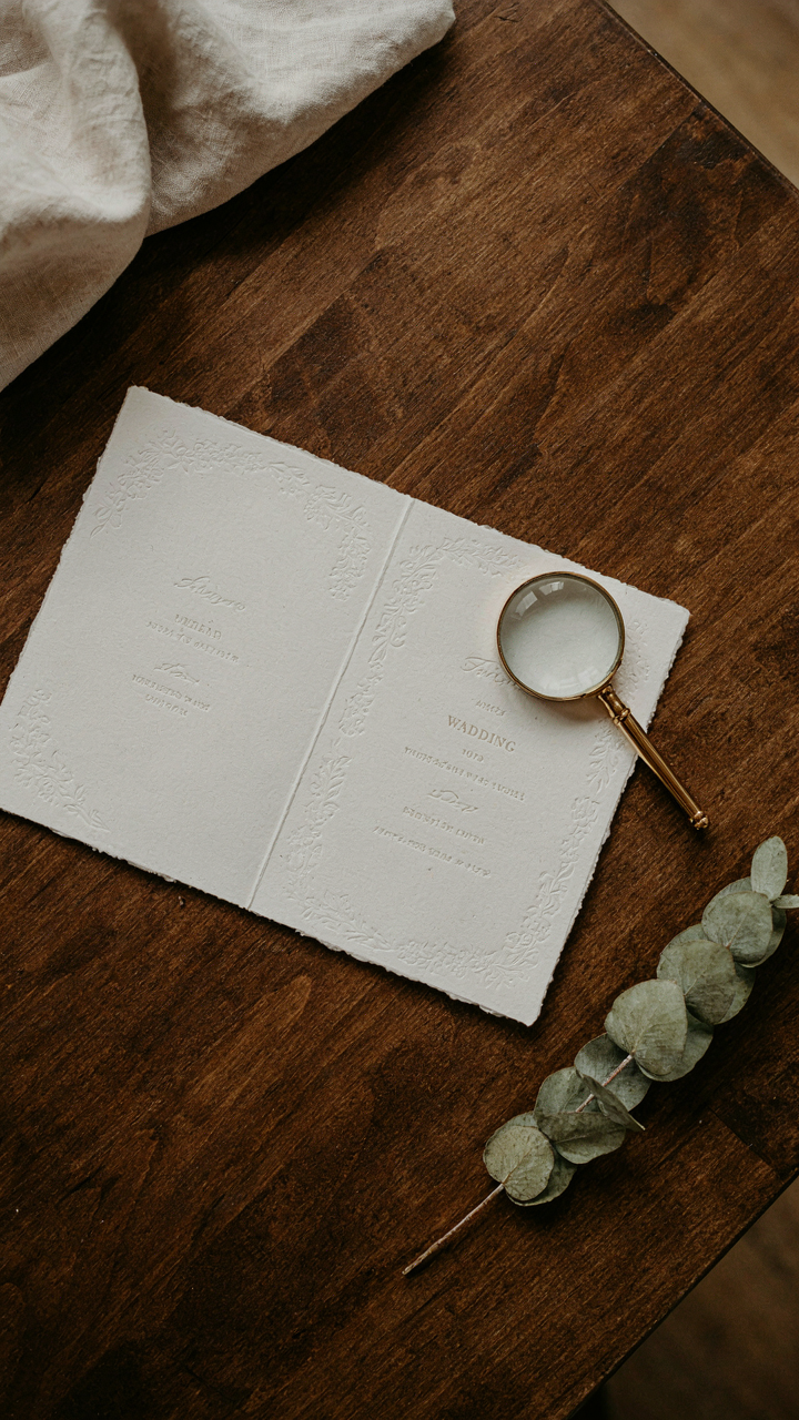 An elegant wedding invitation card is open next to a magnifying glass.