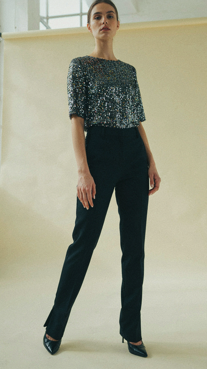 A woman stands tall and confident, her sequin top reflecting light as she moves.