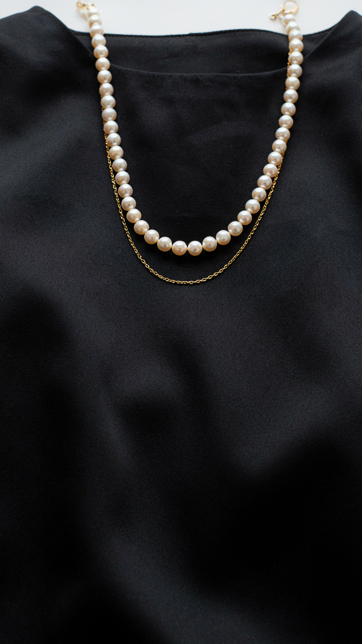 A pearl and a gold chain on a black dress.