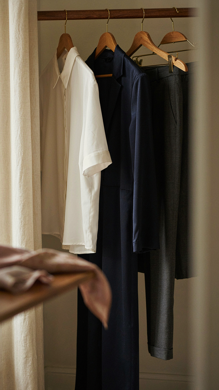 A navy satin jumpsuit hangs in a wardrobe next to a white blouse.