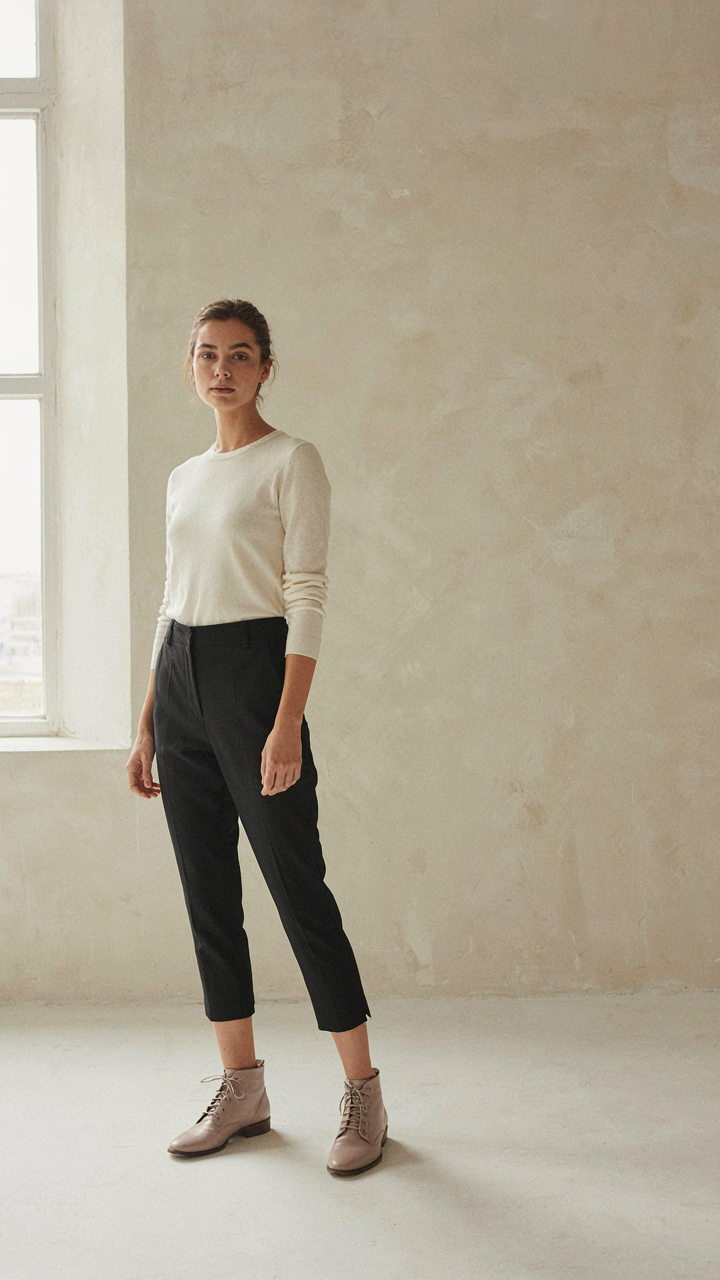 A petite woman in cropped trousers and ankle boots, showing a clean leg line.