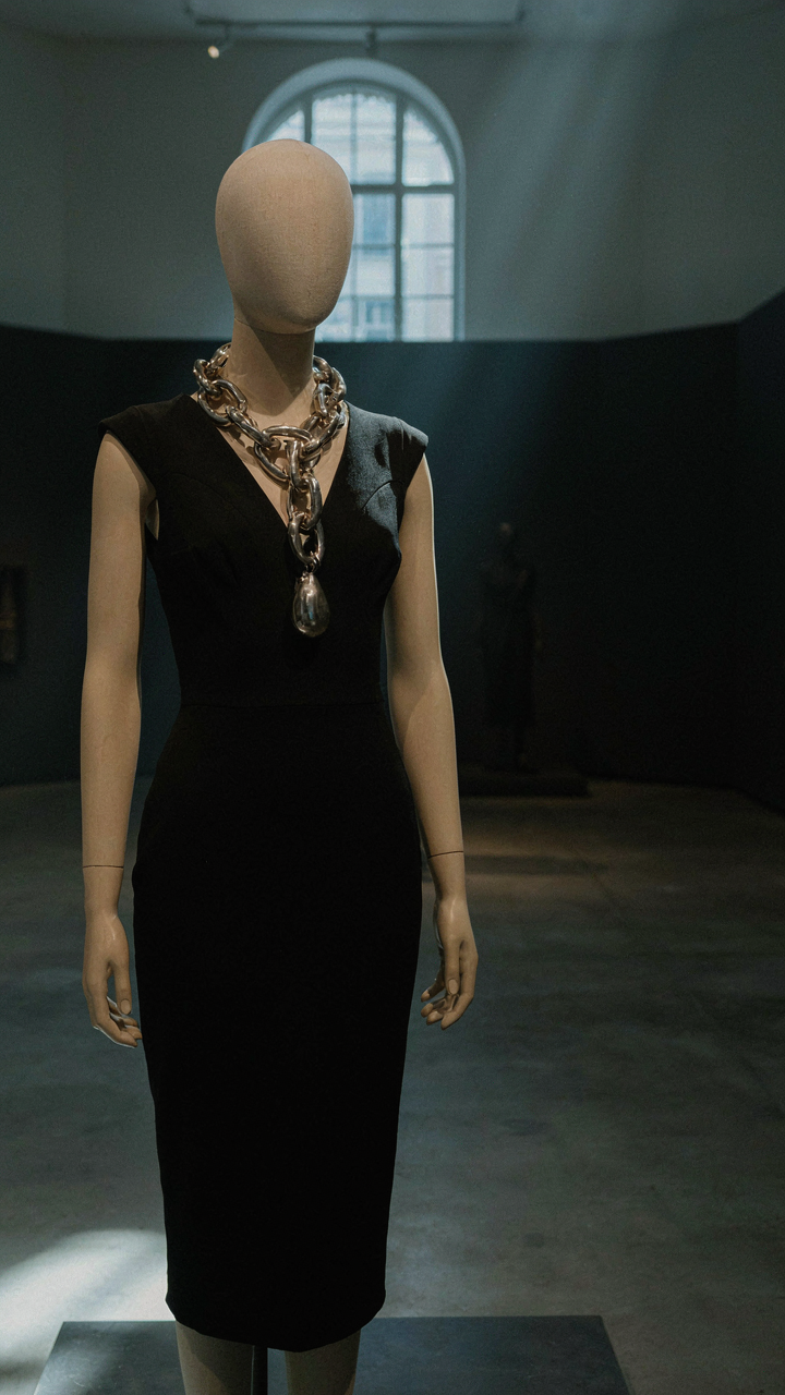 A sculptural statement necklace with cocktail dress on a mannequin in a museum.