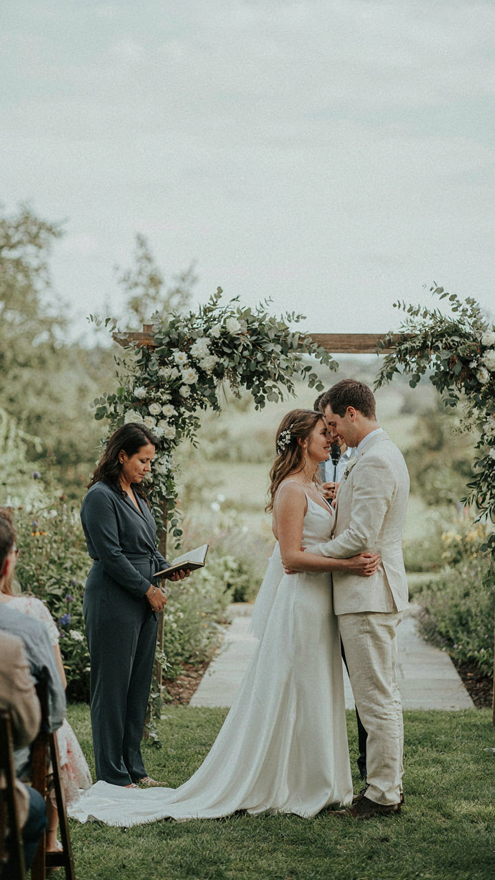 A wedding officiant in a charcoal jumpsuit with sleeves at an outdoor ceremony.