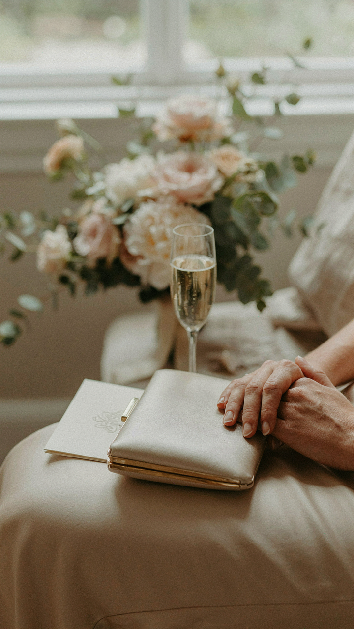 A small, neutral silk clutch rests on a wedding guest's lap.