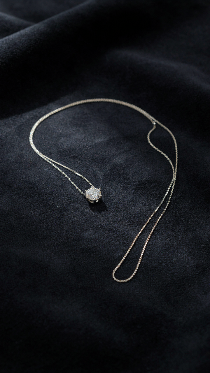 A single diamond pendant necklace rests on dark velvet cloth.
