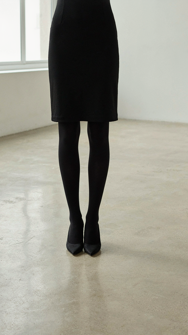 A mannequin wears a cocktail dress and opaque tights, showing a smooth leg line.