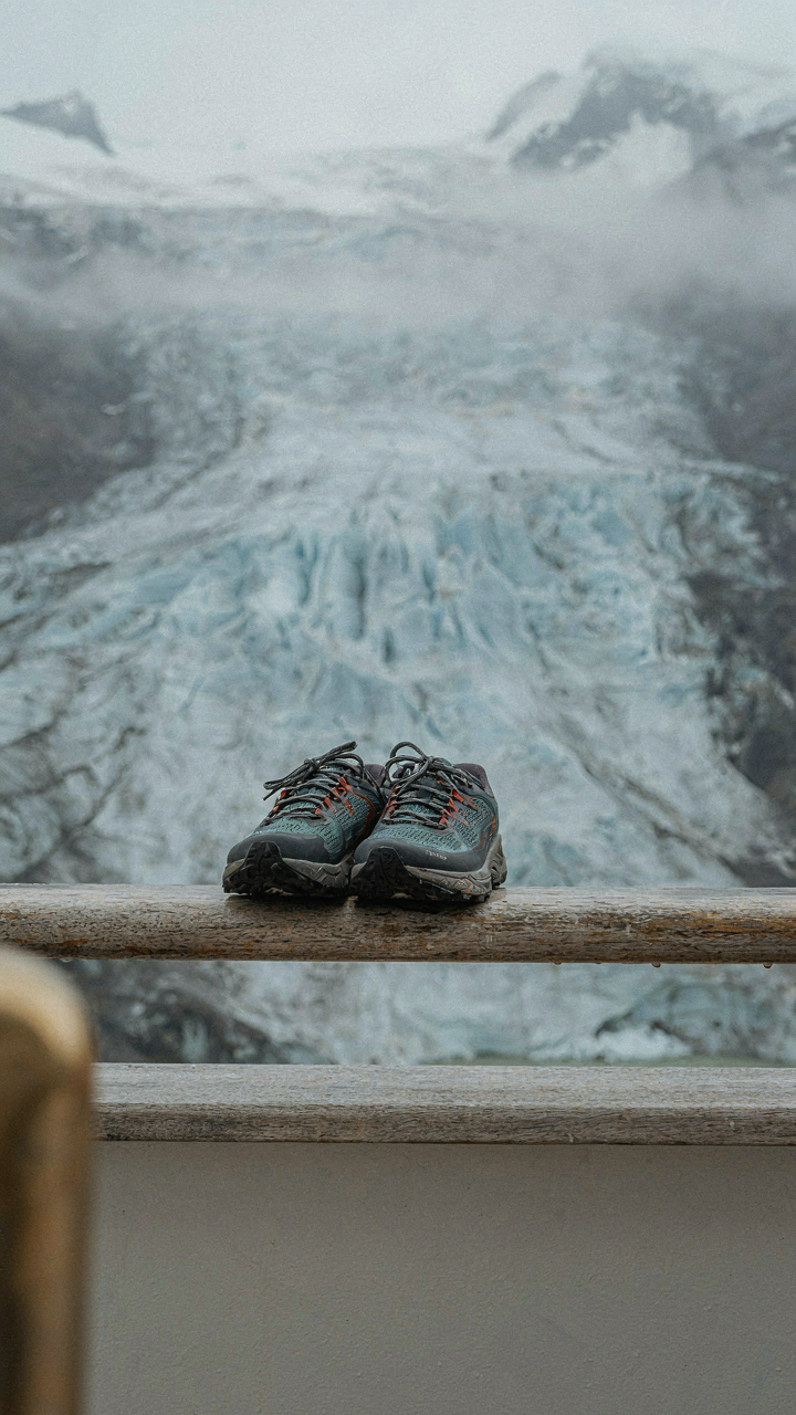Quick-dry shoes sit on a ship's balcony, overlooking a glacier.