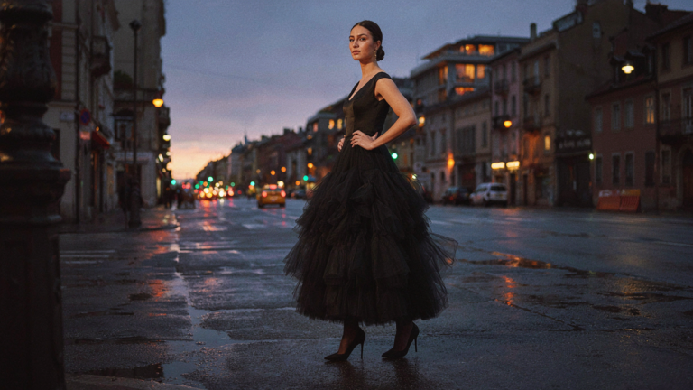 A woman wears a voluminous black tulle skirt evening outfit on a city street at dusk.