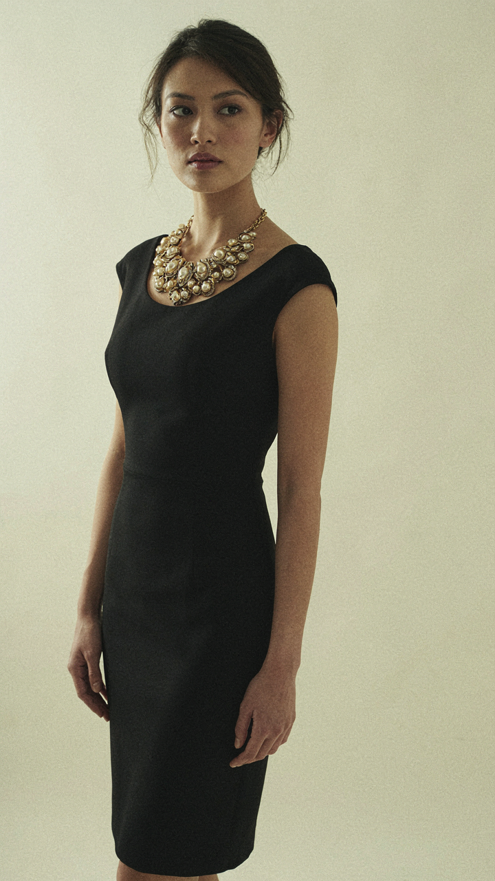A woman confidently wears an ornate statement necklace with a simple dress.