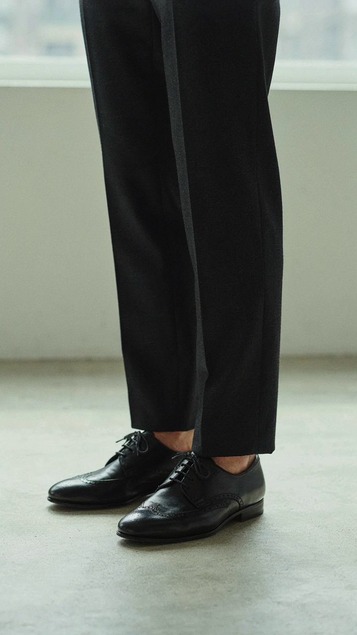 A person wears crisp, tailored trousers and polished formal flats.