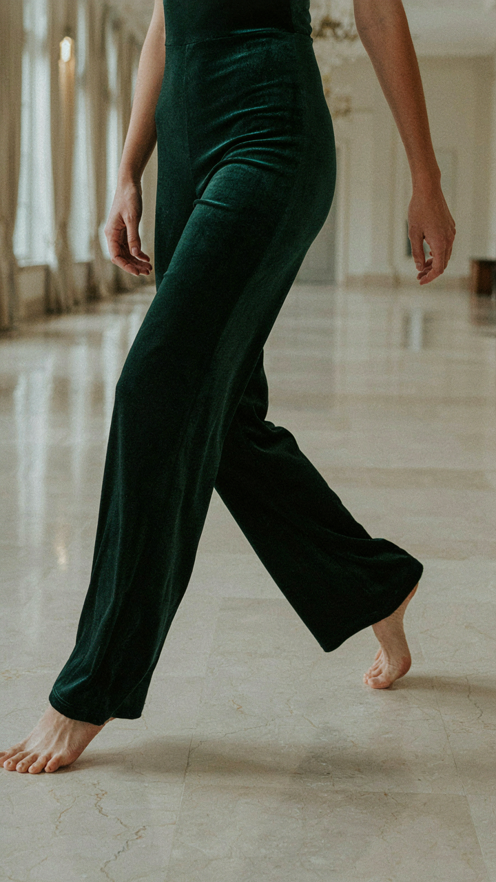 Woman's legs in a velvet jumpsuit taking a deliberate step in a ballroom.