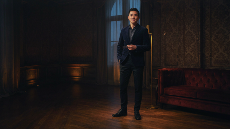 Man in a dark velvet blazer stands confidently in a softly lit, elegant room.