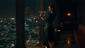 A woman in an emerald velvet cocktail dress sips a drink in a sophisticated lounge.