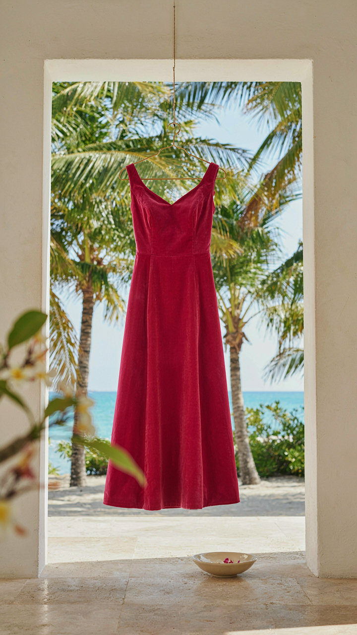 A fuchsia sleeveless cotton velvet dress hangs in a bright tropical setting.