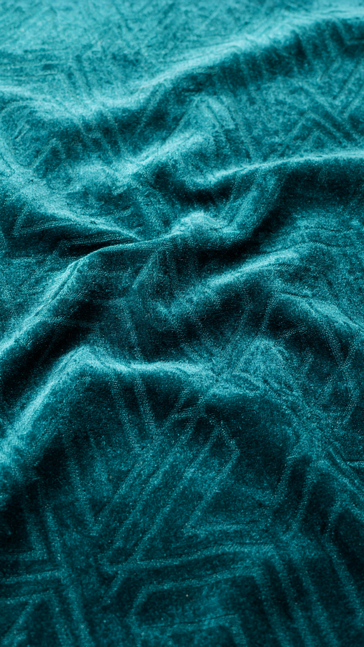 A close-up of deep teal velvet fabric with a subtle art deco pattern.
