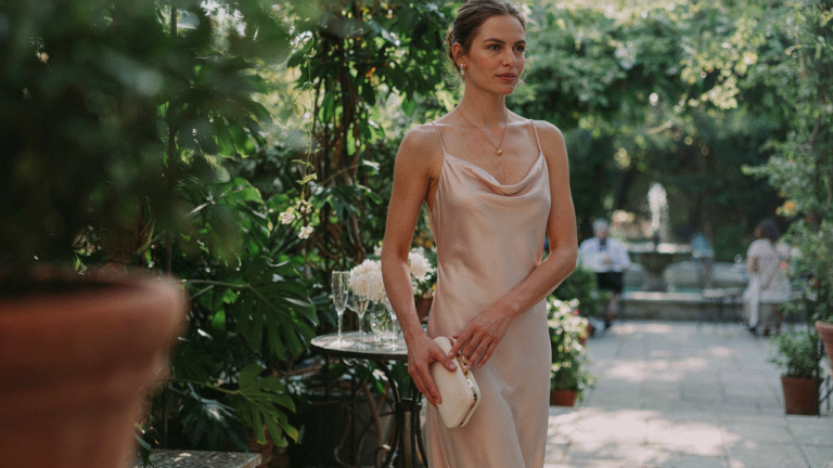 An elegant woman in a sophisticated wedding brunch outfit walks through a sunlit patio.