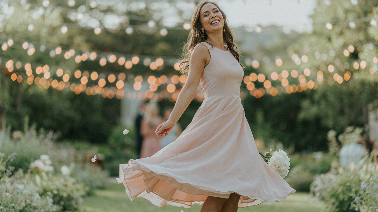 A woman with an apple body shape twirls in a comfortable wedding guest dress.