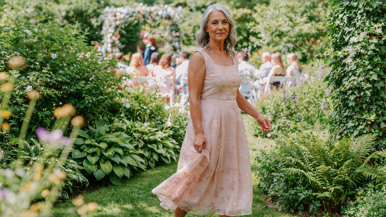 An elegant woman over 60 smiling in a beautiful dress at an outdoor wedding.