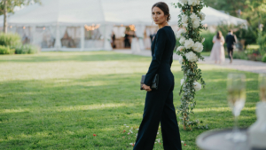A woman wears a dark blue wedding guest jumpsuit at an elegant outdoor event.