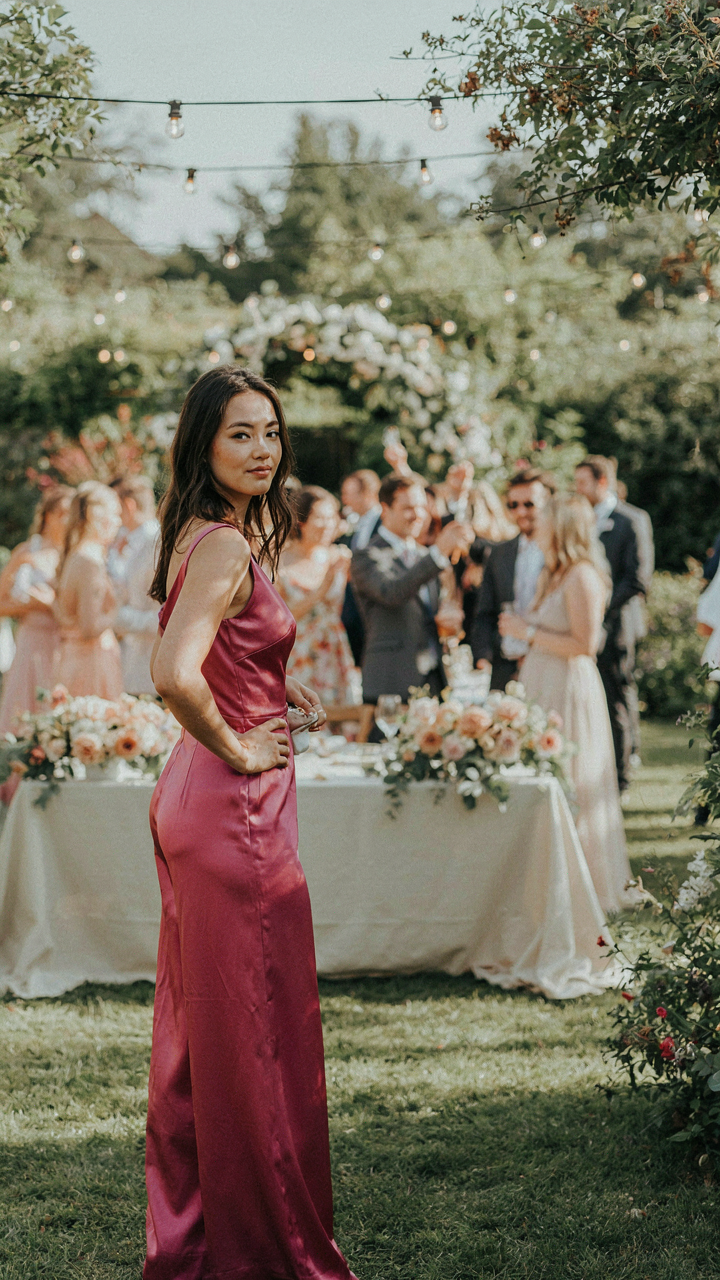 A woman in a fuchsia satin jumpsuit stands out among wedding guests.