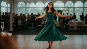 A woman in a flowing jewel-toned dress twirls on a dance floor at a wedding reception.