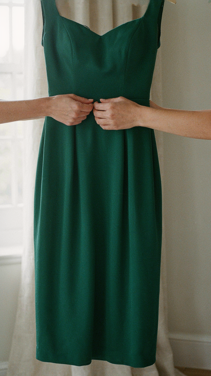 A person's hands smooth out a dark knee-length cocktail dress, showing attention to detail.