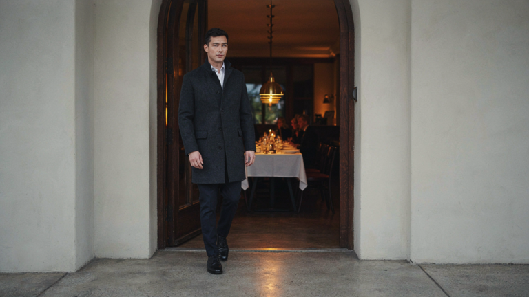 A person in dressy casual clothes confidently enters a fancy restaurant at dusk.