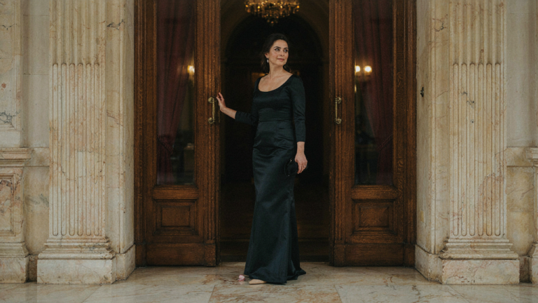 Woman in an elegant dark gown standing at the entrance of a grand event hall.