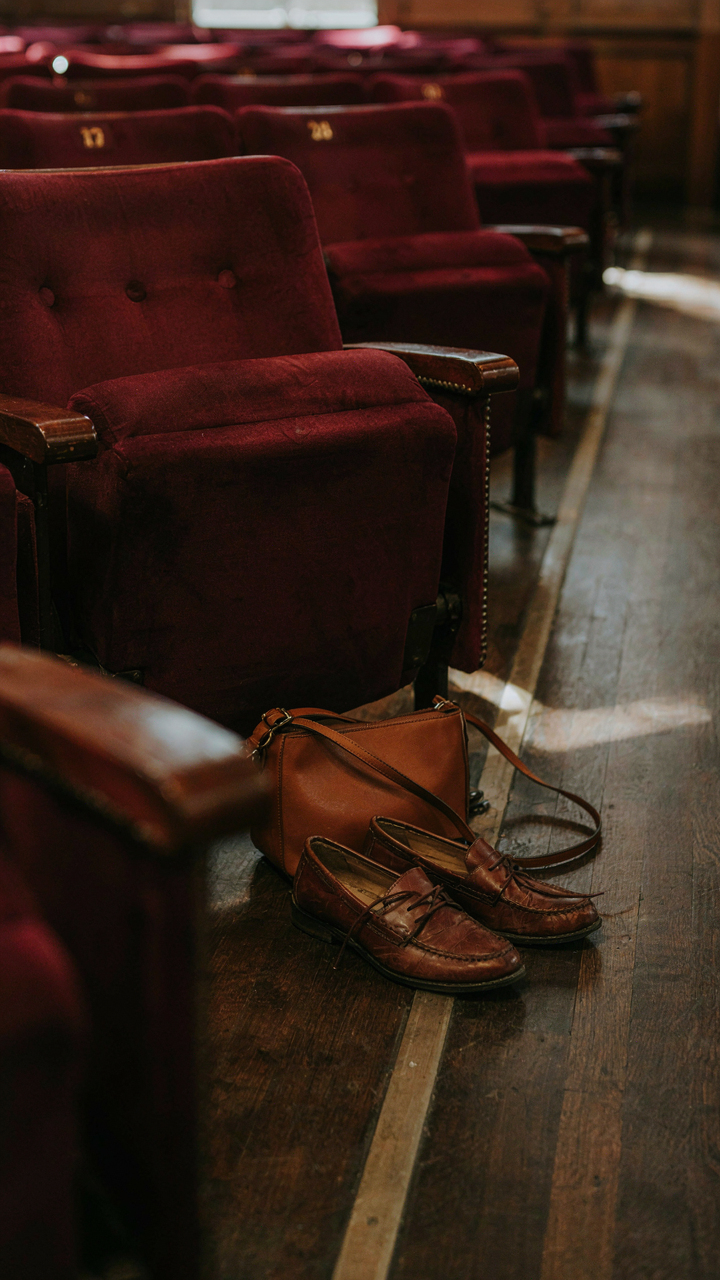 Small crossbody bag and comfortable shoes tucked under a theater seat.